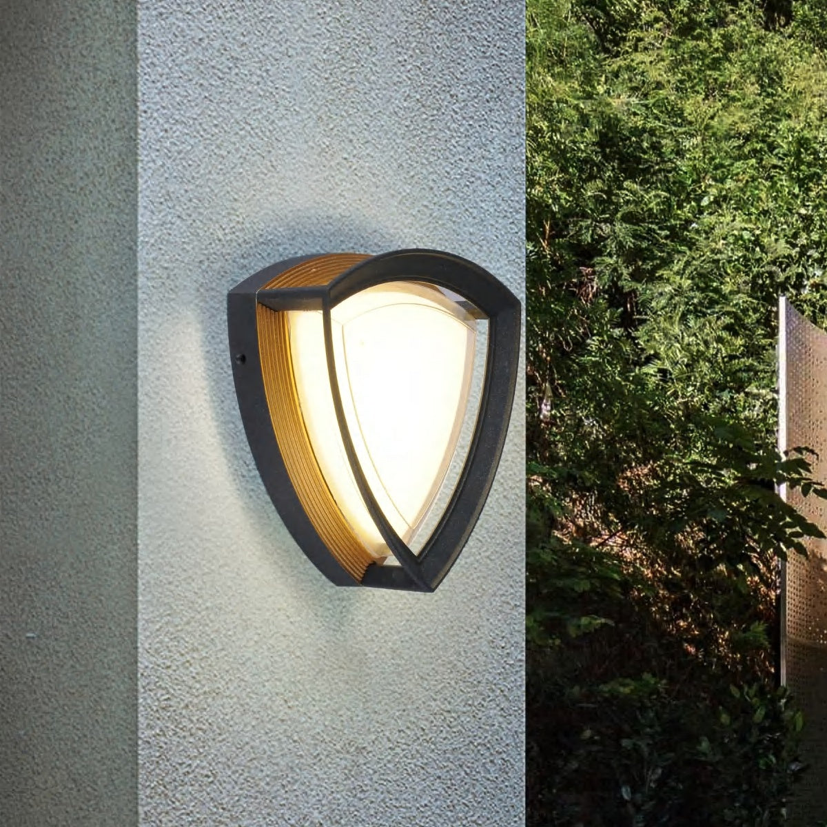AURA Outdoor Wall Light – Shield, Black & Gold (12W, Warm White 3000K) – lit on a wall at dusk